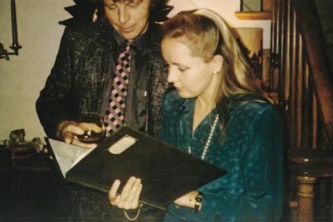 Kaksi henkilö tutkii kansiota. Toisella on kädessään viinilasi.