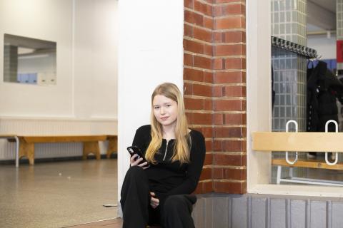 Yläkoululainen istuu sisäportailla puhelin kädessään
