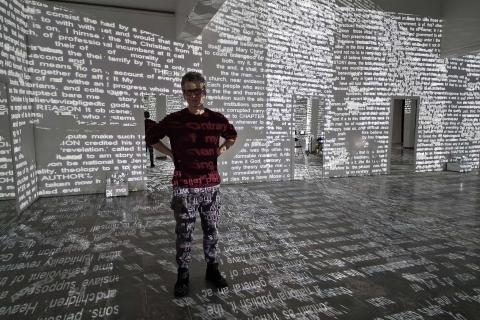 Mies seisoo hämärässä tilassa, jonka seinille on heijastettu sanoja, 