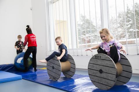 Lapset tasapainottelevat ikkunan edessä isojen rullien päällä. 