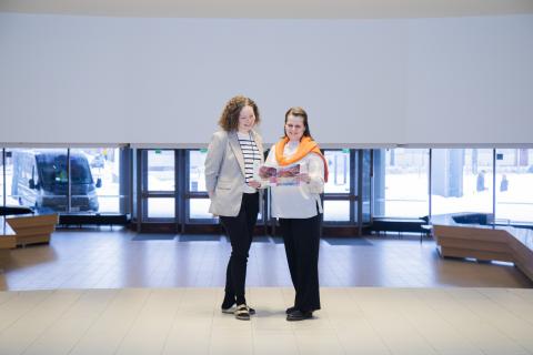 Two people are standing in the spacious lobby of the Workers&#039; College, looking at papers.