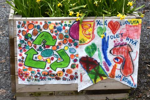 Narsisseja istutuslaatikossa, jonka kyljessä lasten tekemiä julisteita.