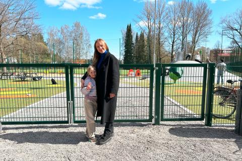 Vanhempi ja lapsi seisovat leikkipuiston porttien edessä.