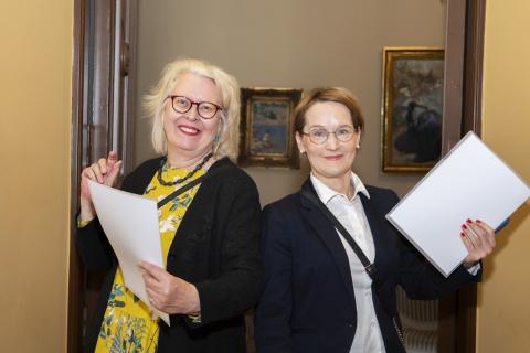 Kaksi naista pitelee edessään papereita.