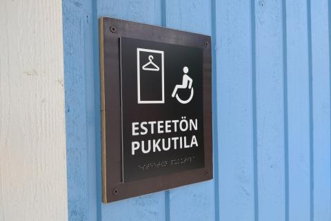 Koho- ja pistekirjoituskyltti Pyynikin esteettömän uimarannan pukuhuoneen seinällä.