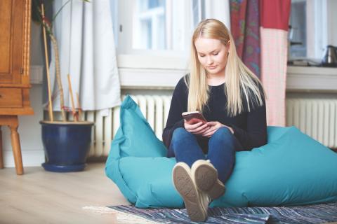 Nuori istuu säkkituolissa ja selaa puhelintaan.