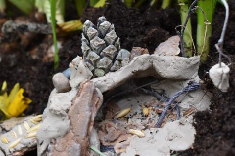 Eskarilaisen savesta, siemenistä ja kävystä tekemä ympäristöteos narsissien juurella.