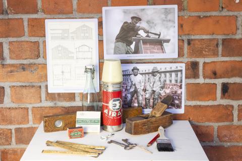 Valokuvia ja rakentajan työkaluja tiiliseinä taustalla.