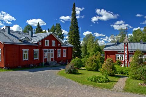 Kaksi punaista vanhaa taloa ja niiden puistomainen piha kauniina kesäpäivänä.
