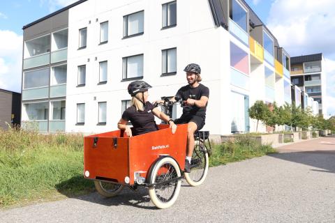 A person riding a three-wheeled cargo bike with another person on board. 
