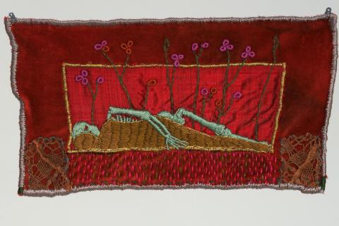 Ristipistotyössä makaa vihreä luuranko punaista taustaa vasten.