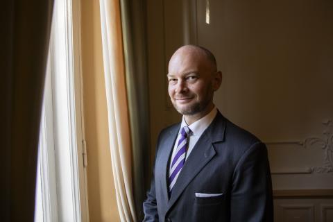 Henkilö seisoo hymyillen ikkunan edessä sivuttain.