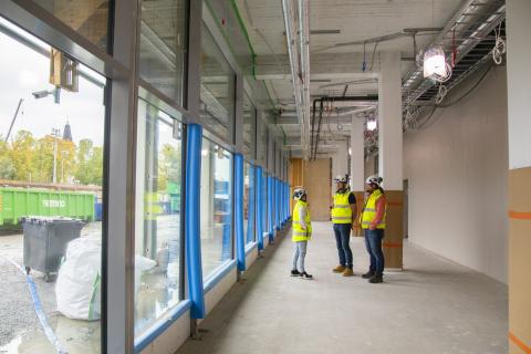 Kolme henkilöä seisoo pitkän ikkunaseinän ja tavallisen seinän välillä juttelemassa keskenään.