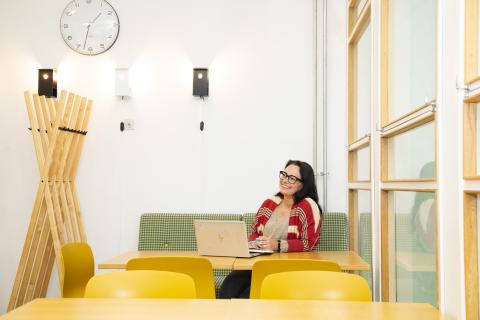 Hymyilevä henkilö istuu pöydän takana läppäri edessään.