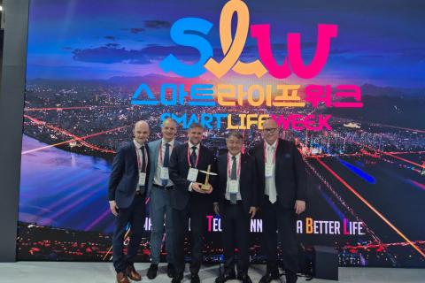 Hymyilevät miehet seisovat rivissä palkintoseinän edessä. 