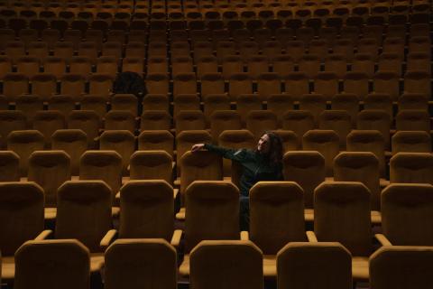 Henkilö istuu yksin puolipimeässä teatterisalissa.