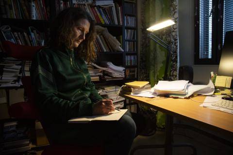 Henkilö istuu hämärässä työhuoneessa kirjoittamassa.