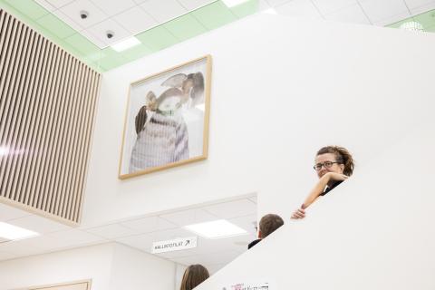 Kaksi oppilasta ja opettaja seisovat portaissa katsomassa lähellä katonrajaa olevaa taulua.