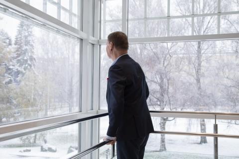 Henkilö seisoo puoliksi selin katsoen ikkunasta lumista maisemaa.