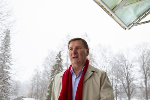 Henkilö seisoo lumisessa maisemassa. Kaulassa punainen huivi. päällä vaalea takki.