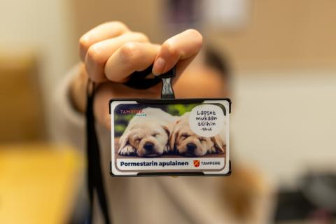 Lähikuva kaulaan ripustettavasta henkilökortista, jossa on kuva kahdesta nukkuvasta koirasta. Tekstissä lukee &quot;Pormestarin apulainen&quot;.