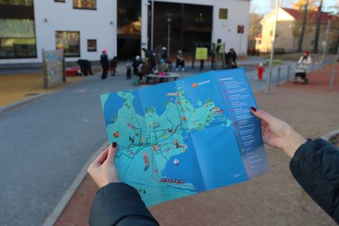 Seikkailukartta lähikuvassa, taustalla päiväkodin pihassa vilskettä.