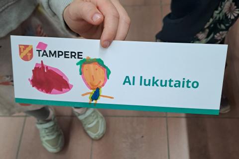 Lapsen käsi pitelee piirrettyä kirjanmerkkiä.