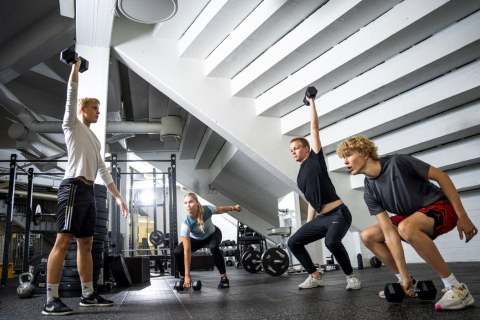 Neljä nuorta urheilijaa tekee käsipainotempauksia oheisharjoittelutilassa.