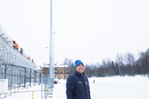 Pipopäinen henkilö seisoo hymyilevänä kentän reunassa lumisessa maisemassa.