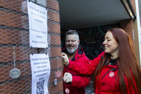 Tullintorin naapurustotyön punatakkiset työntekijät kiinnittävät Tullintorin ulkoseinään hankkeesta kertovaa heijastinta.