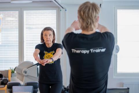 Seniori-ikäinen rouva venyttelee fysioterapeutin esimerkin mukaan.
