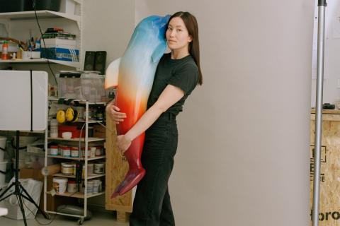 Vuoden nuori taiteilija 2025 Man Yau halaa värikästä delfiiniveistosta työhuoneellaan.