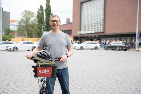 Henkilö rautatieaseman edustalla kaupunkipyörän kanssa.