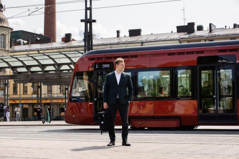 A person looks to the side on Hämeenkatu, with a tram and bus shelter behind them.