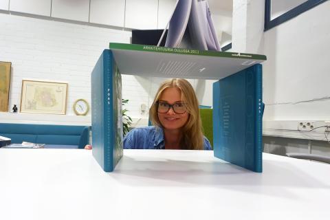 Helmi Haapalainen kurkistaa kirjarakennelman välistä kahvihuoneessa.