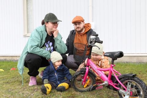 Kaksi aikuista ja kaksi lasta päiväkodin pihassa lapsen polkupyörän kanssa.