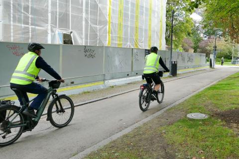 Kaksi pysäköinnintarkastajaa pyöräilevät katua pitkin.