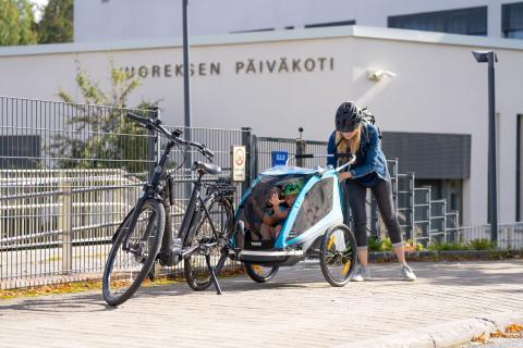 Henkilö laittaa lapsia pyöräperäkärryn kyytiin päiväkodin pihassa.