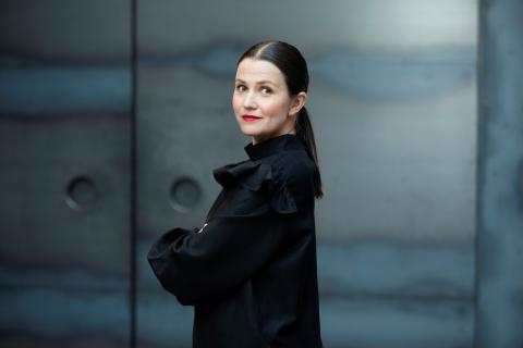 Kaisa Happonen seisoo sinertävän seinän edessä. 