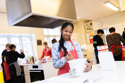 Henkilö sekoittaa kulhossa olevia aineita. Taustalla on muita oppilaita työn touhussa.