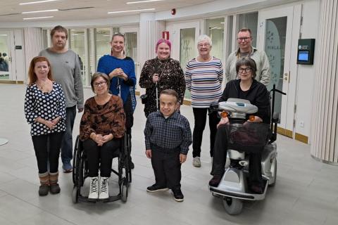 Esteettömyystyöryhmän kahdeksan jäsentä sekä esittelijä seisovat ryhmäkuvassa. Osa jäsenistä istuu pyörätuolissa.