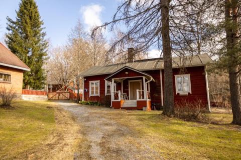 Kuvassa punamultamaalilla maalattu vanha omakotitalo, jossa on valkoiset ikkunanpuitteet. Etualalla havupuita.