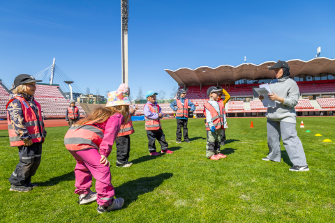 Seven children play on the grass field of the Ratina stadium, following teacher Sumaya Haidarian's instructions.
