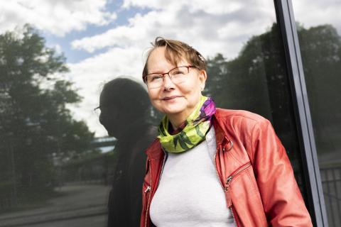Punaiseen takkiin ja vihreään huiviin pukeutunut yliopistonlehtori Tuula Juvonen seisoo ulkona ikkunan luona. Ikkunasta heijastuu hänen varjokuvansa.