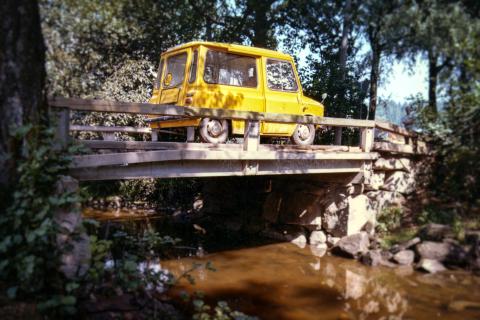 Vanha keltainen postin auto ajaa pienellä sillalla joen yli