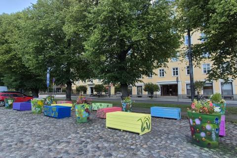 Värikkäitä puulaatikoita ja isoja kasviruukkuja viherkasviteemaisilla maalauksilla Pyynikintorin mukulakivetyksellä.