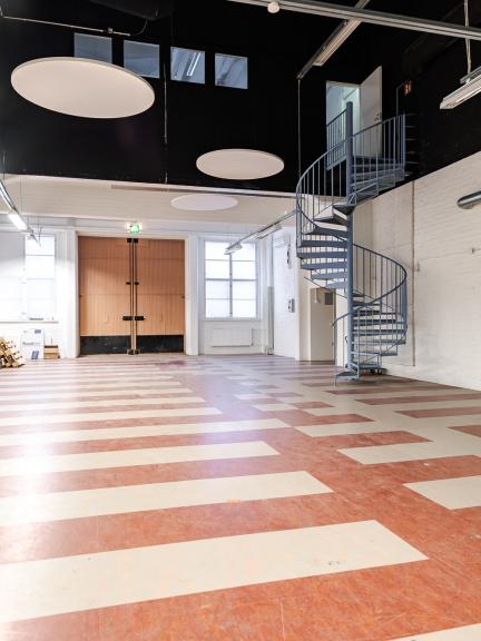 Sisäkuva rollikkahallin aulasta. takaseinällä iso pariovi ja ovien lähellä metalliset kierreportaat.