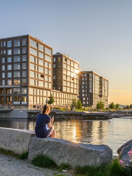 Nainen istuu rantakivillä Ranta-Tampellassa. Taustalla näkyy rantaviivaa ja kerrostaloja.