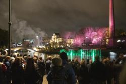 Paljon ihmisiä takaapäin kuvattuna seisomassa ja katsomassa Valoviikkojen avajaisten Tanssivat vedet -suihkulähdeteosta, joka taustalla vihreinen valoineen. Hämeensilta, Tampereen teatteri ja Vanha kirjastotalo valaistuna.