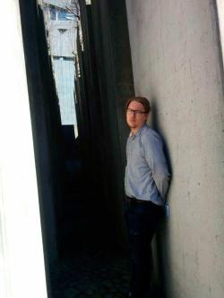 Silmälasipäinen mies nojaa betoniseinään. 